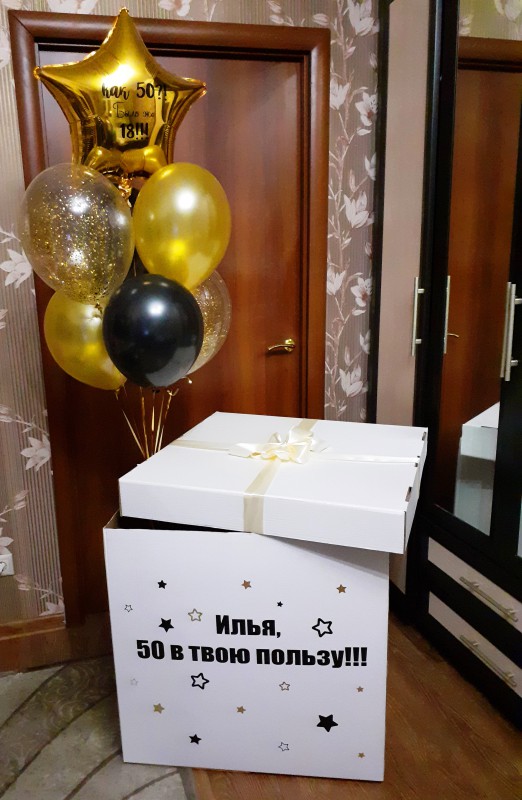 Большая коробка-сюрприз с надписью "Илья, 50 в твою пользу!!!" и с фонтаном из гелиевых шаров чёрно-золотой 